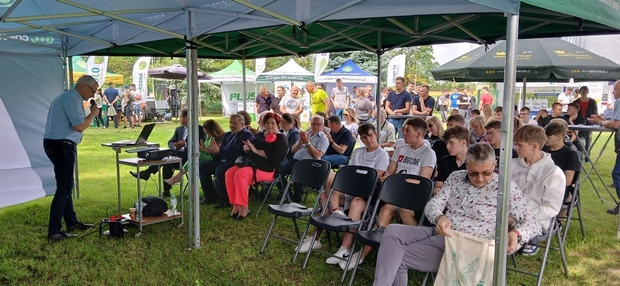 Na zdjęciu widać liczną grupę uczestników Dni Pola. Siedzą pod namiotem na krzesłach, słuchają wystąpienia Dyrektora Stacji Doświadczalnej Oceny Odmian w Krzyżewie.